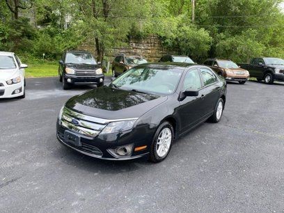 Black sedan parked in an outdoor lot with other cars and greenery in the background.