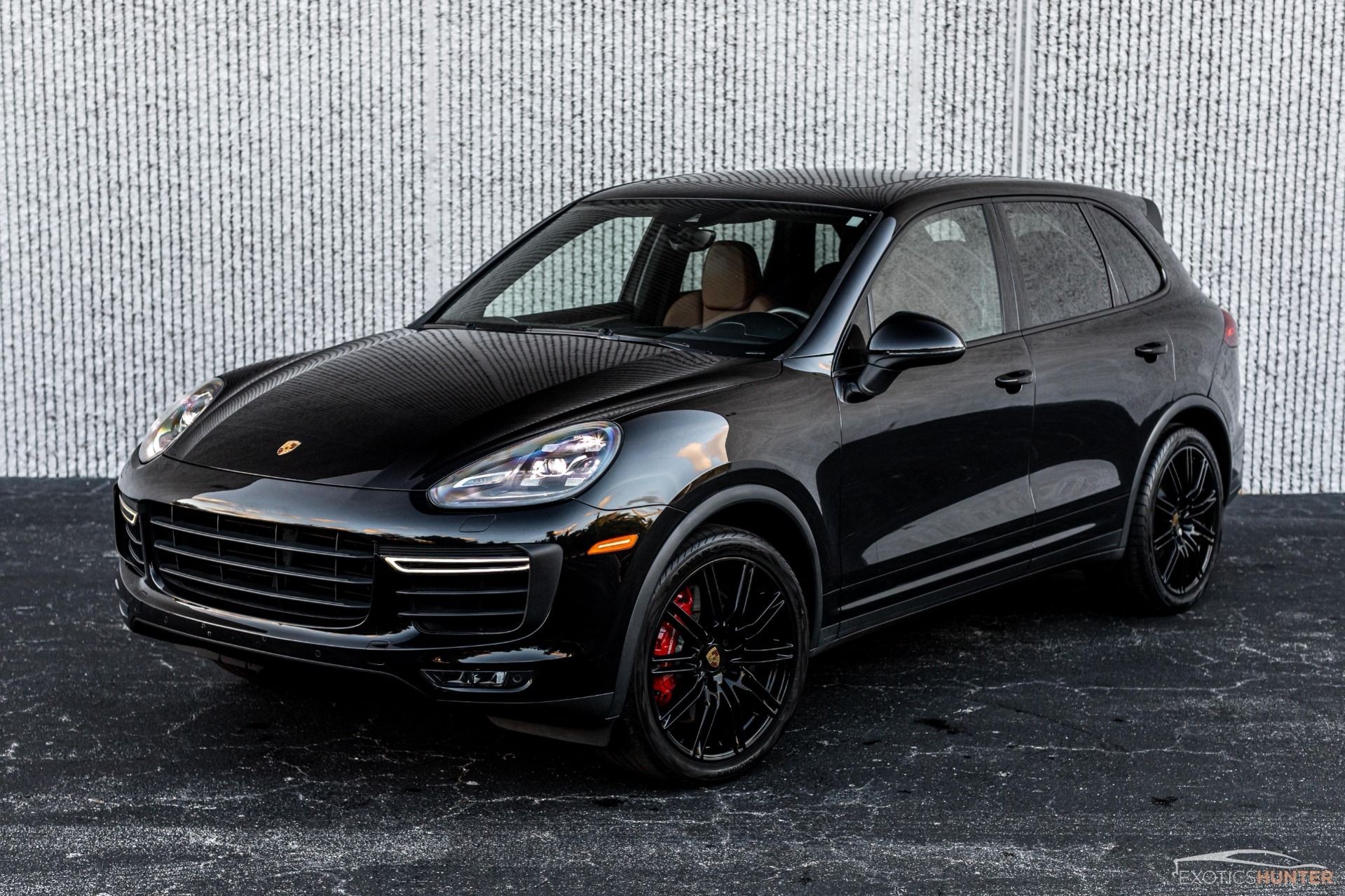 Black luxury SUV with sleek design, parked on a textured ground against a white patterned wall.